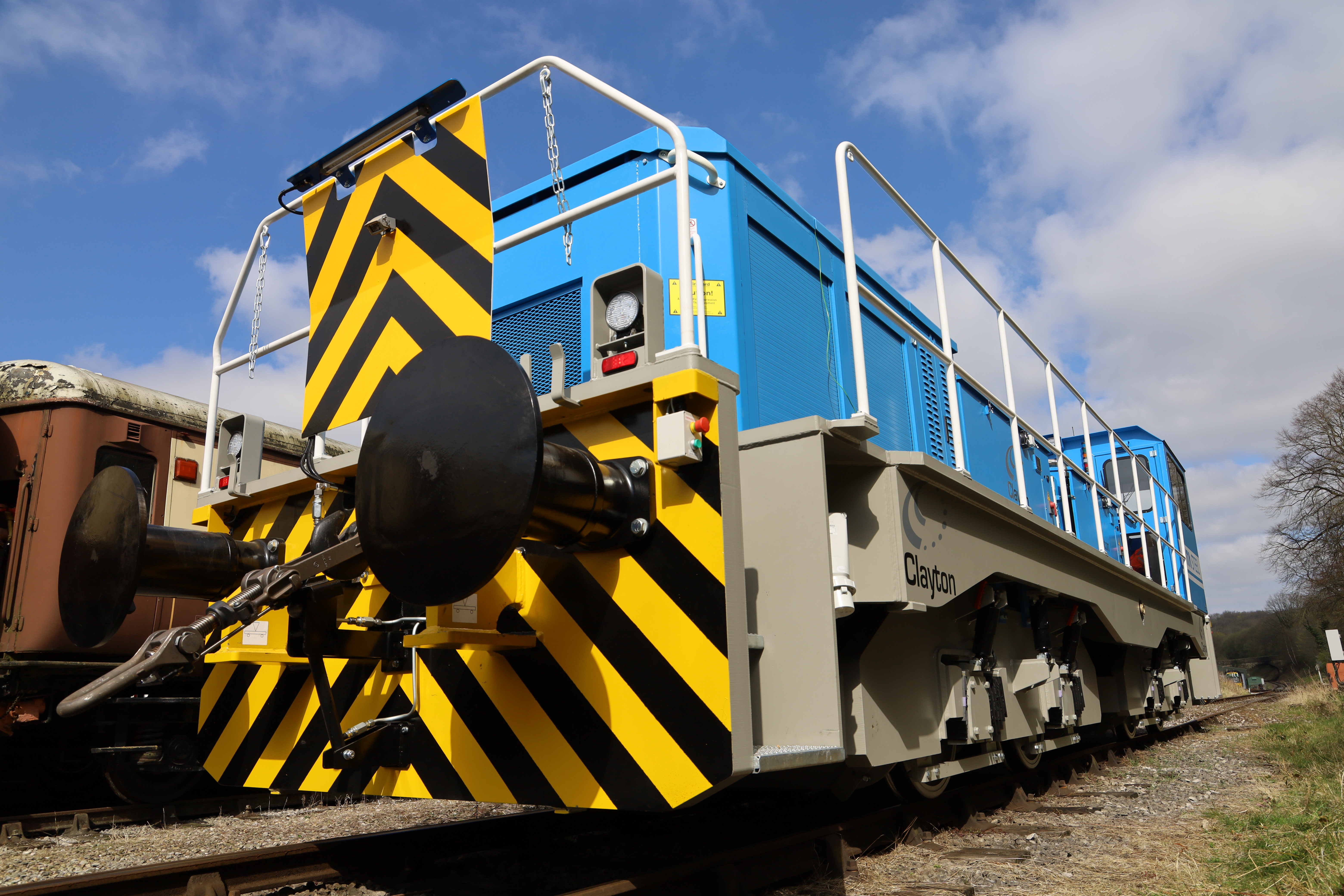 Zero-emission battery-electric locomotive by Clayton, featuring bold safety striping and modern design, positioned on a railway track under a blue sky — symbolising sustainable rail transport solutions.